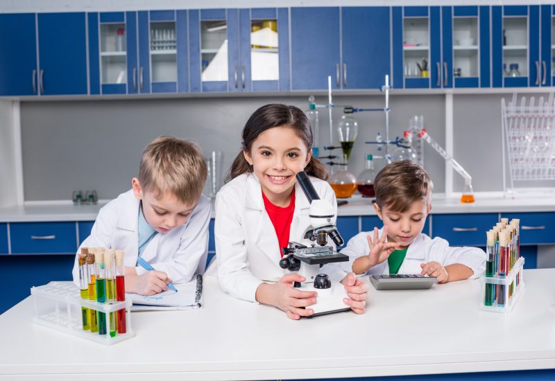 three-kids-in-chemical-laboratory-making-notes-and-using-microscope-and-calculator.jpg